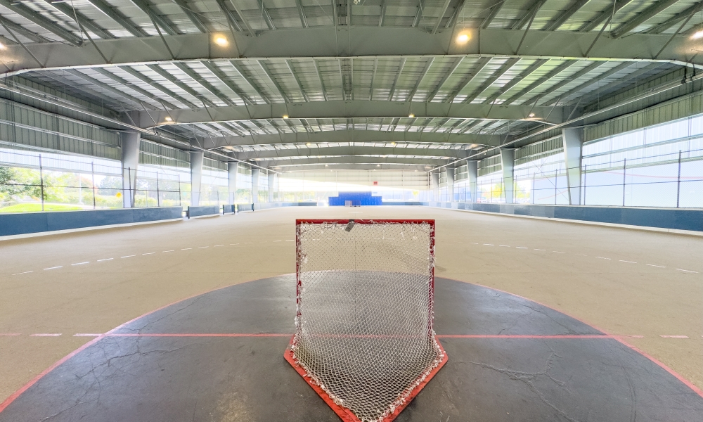 Point of view photo from behind a lacrosse net, overlooking the Ladner Leisure Centre Covered Multi-Sport Court.