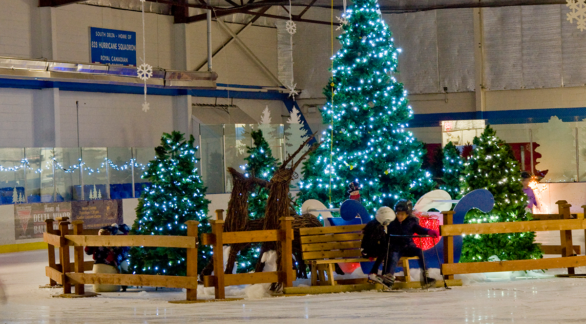 A pair of skaters sit on a bench in the middle of a seasonally-themed skating rink.